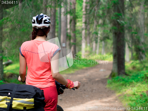 Image of Woman riding a bike on the forest trail in sunny day