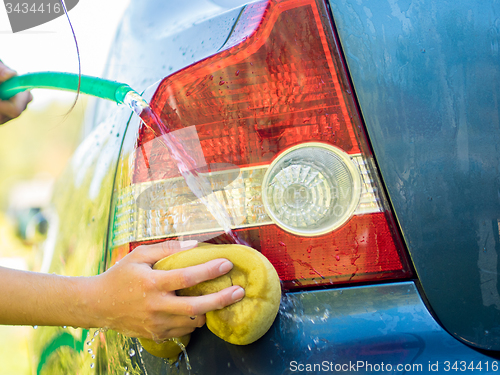 Image of Hand washing rear lights of blue car by sponge