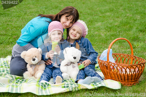 Image of Mum embraces daughters on a picnic