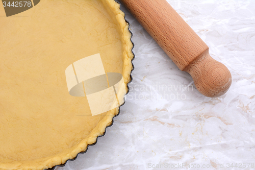 Image of Baking tin lined with pastry, wooden rolling pin beside