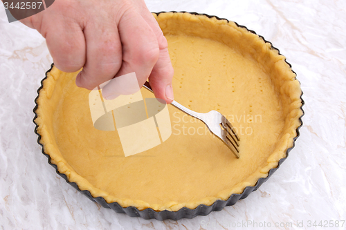 Image of Woman using fork to prick holes in an uncooked pie crust