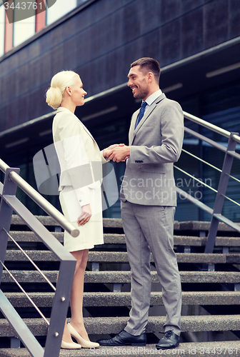 Image of smiling businessmen shaking hands on street