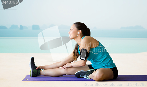 Image of smiling woman stretching leg on mat over pool