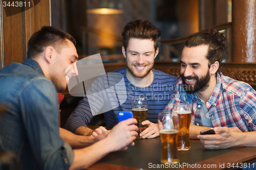 Image of male friends with smartphones drinking beer at bar