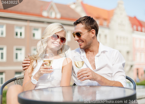 Image of smiling couple in sunglasses drinking wine in cafe