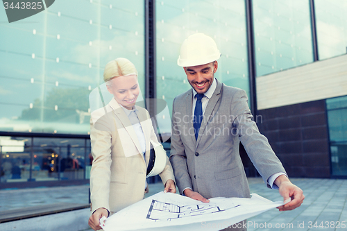 Image of smiling businessmen with blueprint and helmets