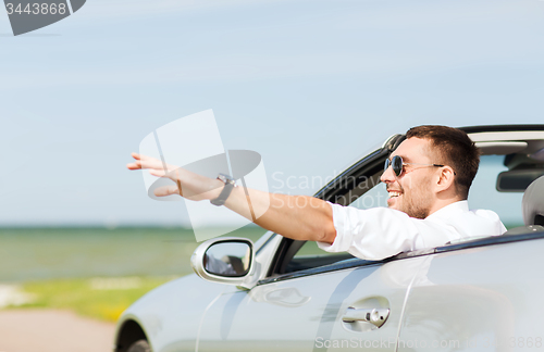 Image of happy man driving cabriolet car and waving hand