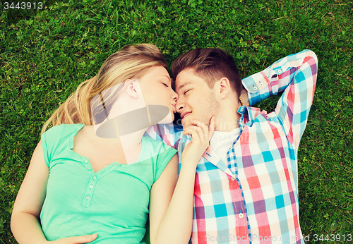 Image of smiling couple lying on grass and kissing in park