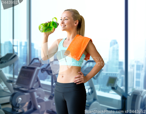 Image of happy woman drinking water from bottle in gym