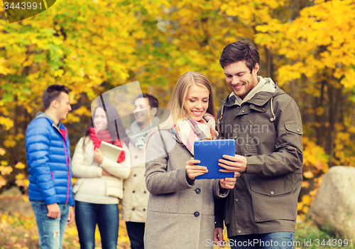 Image of group of smiling friends with tablets in park