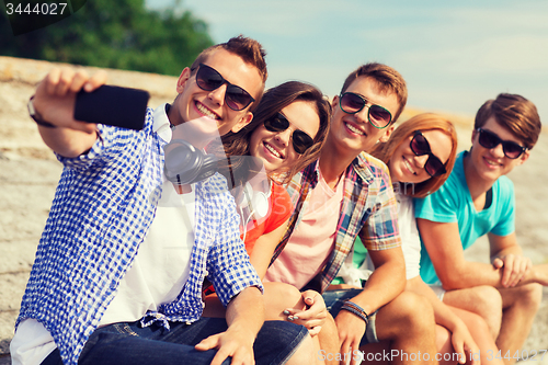 Image of group of smiling friends with smartphone outdoors