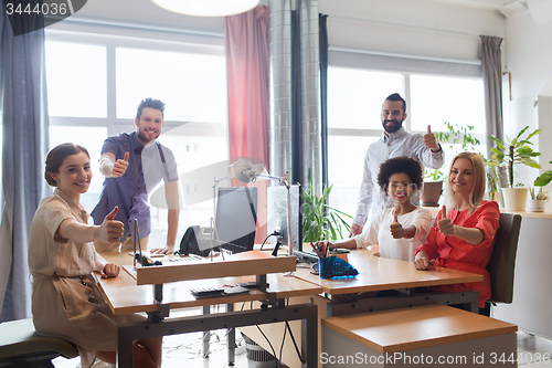 Image of happy creative team showing thumbs up in office