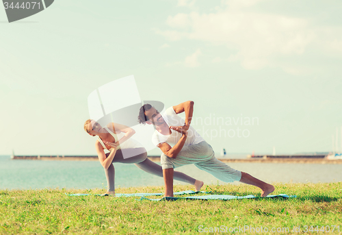 Image of smiling couple making yoga exercises outdoors