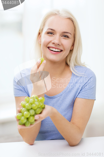 Image of happy woman eating grapes at home