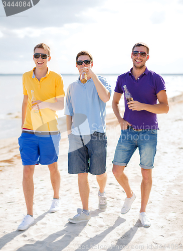 Image of happy friends drinking beer and walking on beach