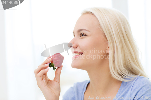 Image of happy woman eating strawberry at home
