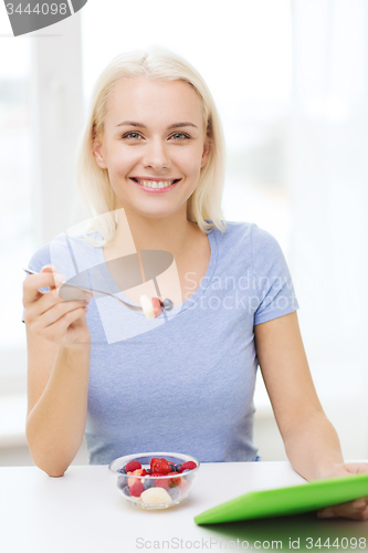 Image of smiling woman eating fruits with tablet pc at home