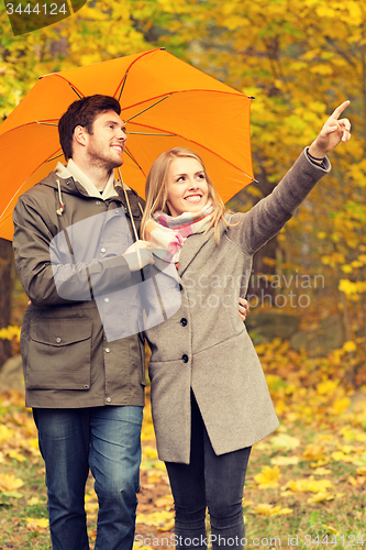 Image of smiling couple with umbrella in autumn park