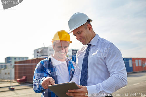 Image of happy builders in hardhats with tablet pc outdoors