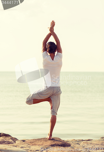 Image of young man making yoga exercises outdoors