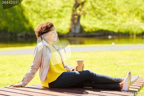 Image of happy african woman drinks coffee at summer park 