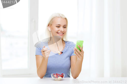 Image of woman with smartphone eating fruits at home