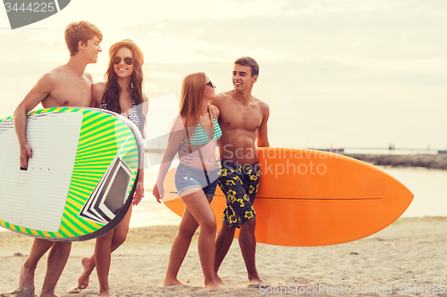 Image of smiling friends in sunglasses with surfs on beach