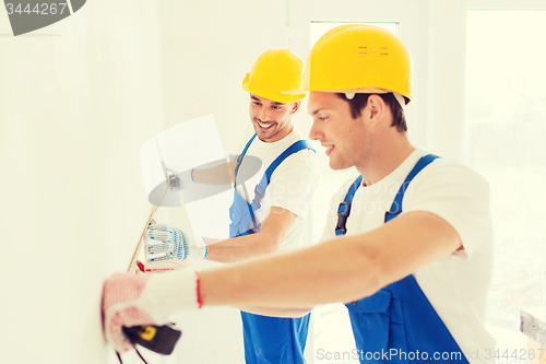 Image of smiling builders with measuring tape indoors