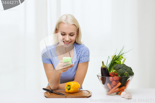 Image of smiling woman with smartphone cooking vegetables