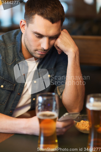 Image of man with smartphone drinking beer at bar