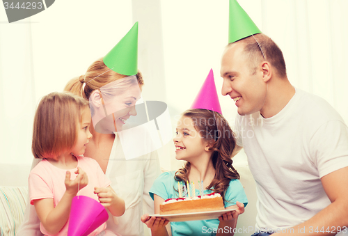 Image of smiling family with two kids in hats with cake