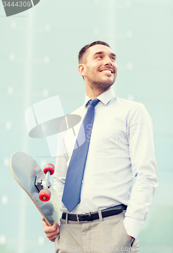 Image of young smiling businessman with skateboard outdoors