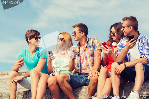 Image of group of smiling friends with smartphones outdoors