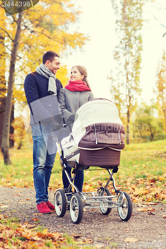 Image of smiling couple with baby pram in autumn park