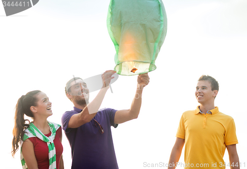 Image of happy friends with chinese sky lantern on beach