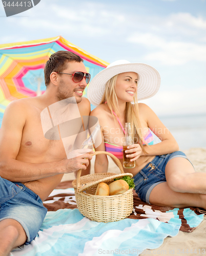 Image of happy couple having picnic and sunbathing on beach