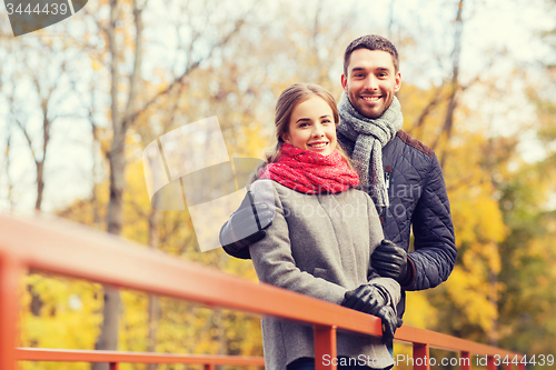 Image of smiling couple hugging on bridge in autumn park