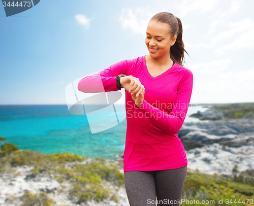 Image of smiling woman with heart rate watch on beach