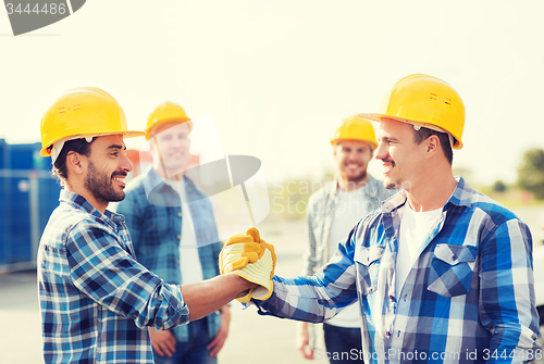 Image of group of smiling builders shaking hands outdoors