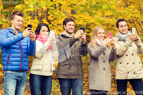 Image of smiling friends with smartphones in city park