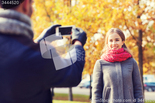 Image of smiling couple with smartphone in autumn park