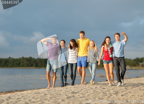 Image of group of happy friends walking along beach