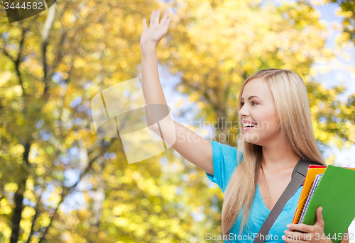 Image of student with folders waving hand over autumn park