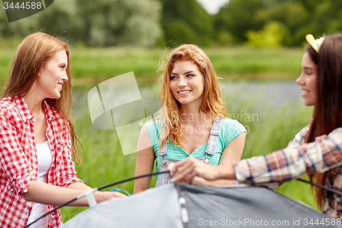 Image of group of smiling friends setting up tent outdoors