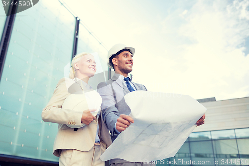 Image of smiling businessmen with blueprint and helmets