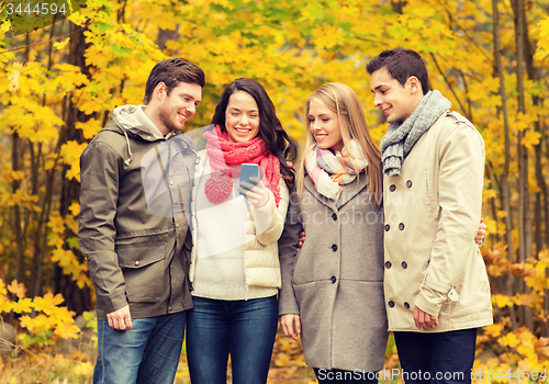Image of smiling friends with smartphones in city park
