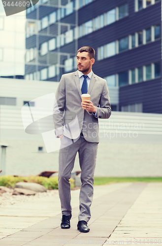 Image of young serious businessman with paper cup outdoors