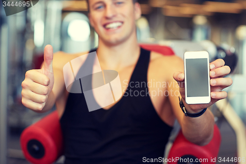Image of young man with smartphone showing thumbs up in gym