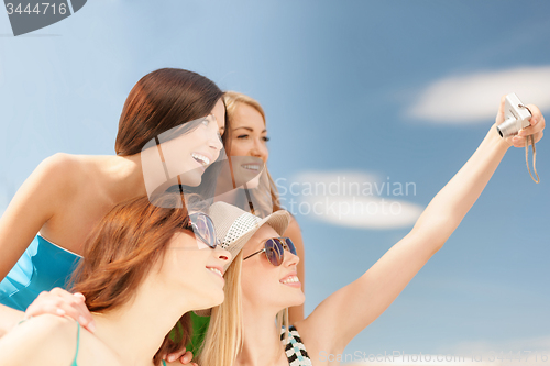 Image of smiling girls taking photo in cafe on the beach