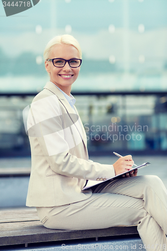 Image of young smiling businesswoman with notepad outdoors